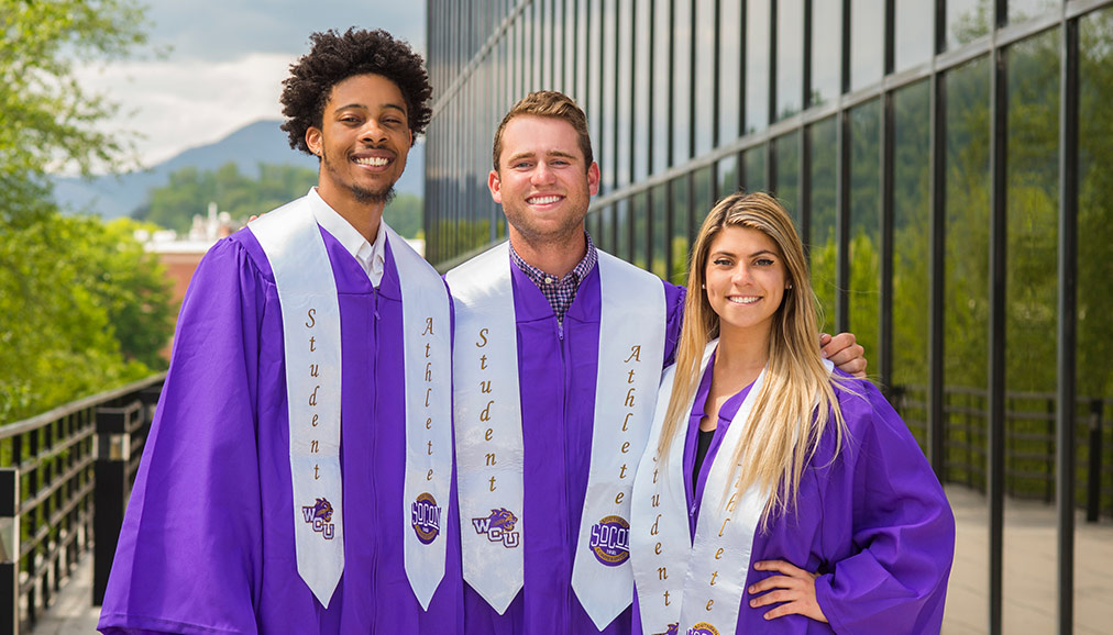 Three student athletes wearing graduation robes.