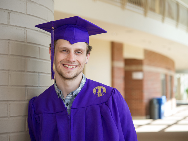 Scholarship recipient Briar Boggs posing in the Bardo Fine and Performing Arts Center decked to the nines in his purple cap and gown.