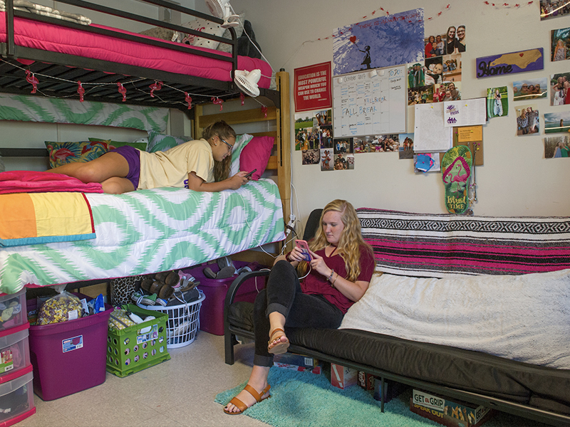 Two female students on their phones hanging out in their room in Reynolds Hall.