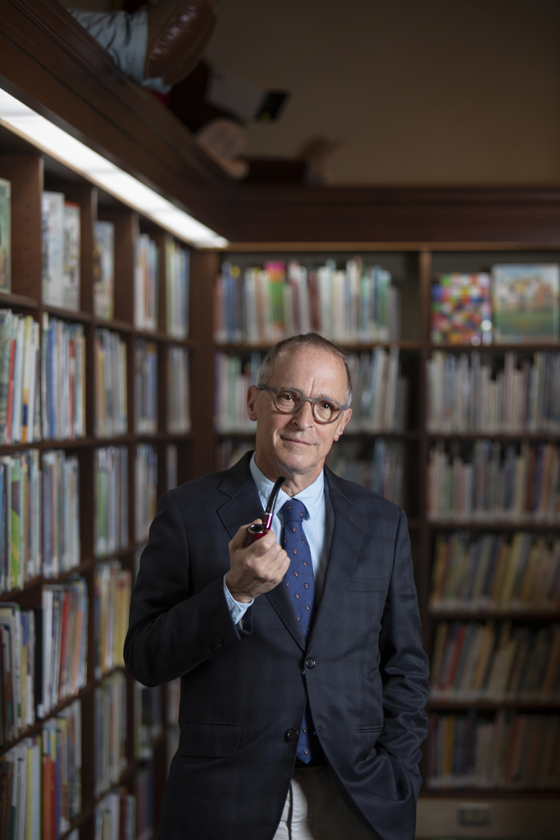 David Sedaris in a suite holding a pipe in a library.