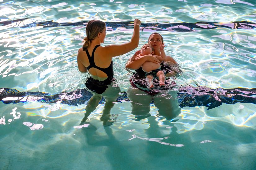 A swim instructor working with a parent and infant