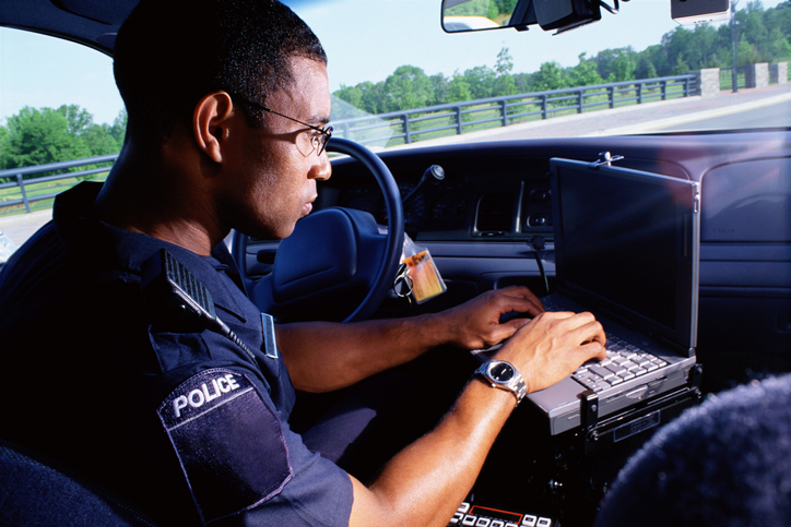 Police officer typing on laptop in patrol car