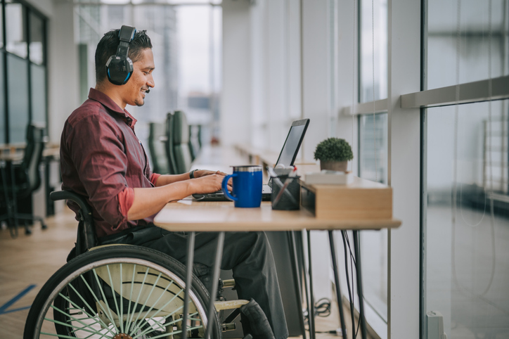 Man in wheelchair at desk working on laptop and smiling