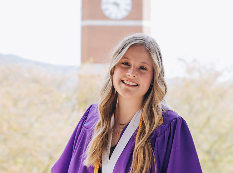 Alexis Moser dressed in graduation regalia in front of the alumni tower