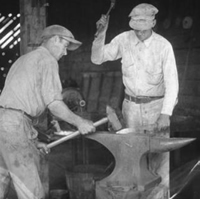 Smith (at right) and striker (at left) hammer hot metal on an anvil